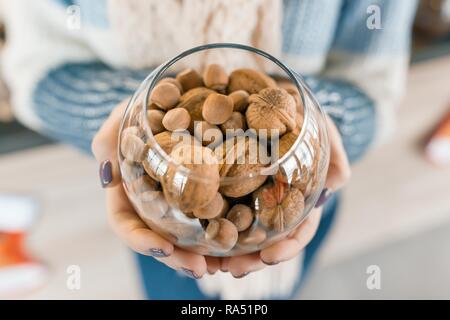 Primo piano del vaso di vetro con i dadi - e le nocciole nonché le noci comuni nelle mani della donna. Foto Stock