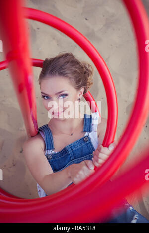 Adorabile signora giovane ragazza teen può biondino di castagno con deep blue eyes giocando in posa sul parco giochi per bambini sabbia jeans blu ponticello camicia bianca happ Foto Stock