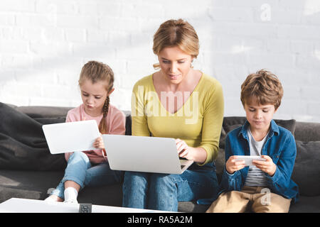 Madre e bellissimi bambini utilizzando dispositivi digitali a casa Foto Stock