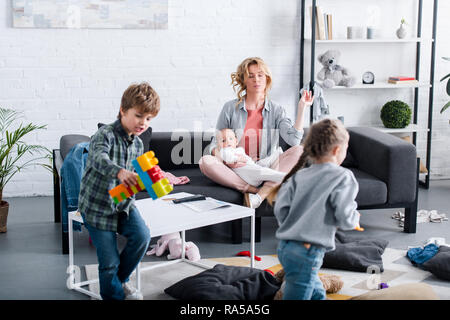 Madre con bambino neonato meditando nella posizione del loto mentre naughty fratelli giocare in casa Foto Stock