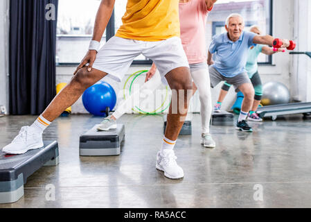 Ritagliato colpo di atleti senior esercizio sincrono con manubri in fase di piattaforme in palestra Foto Stock