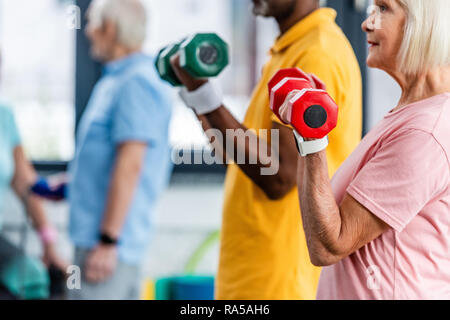 Vista parziale di interracial coppia matura fare esercizio con manubri in palestra Foto Stock