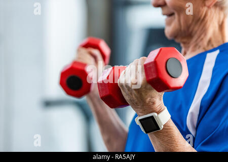 Vista parziale di di senior sportivo con smartwatch fare esercizio con manubri in palestra Foto Stock