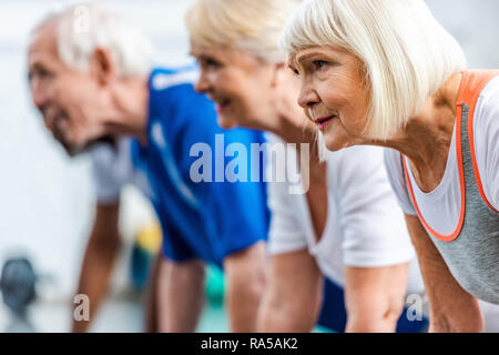 Messa a fuoco selettiva di senior sportive e i suoi amici facendo Plank in palestra Foto Stock