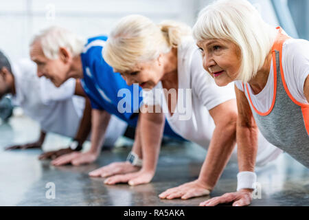 Messa a fuoco selettiva di senior sportive e i suoi amici facendo Plank in palestra Foto Stock