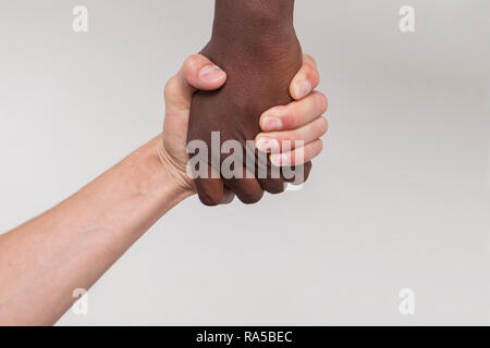 Fotografia concettuale. Due bracci. Un americano africano o africano aiuta un bianco-scuoiati persona stand o a salire. Aiuto o di amicizia tra il popolo. Foto Stock