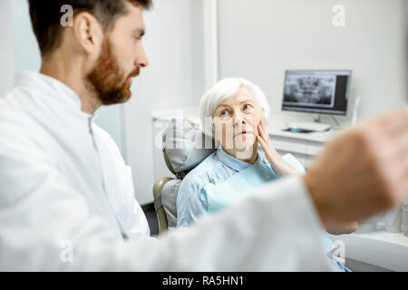 Preoccupato elder donna durante la consultazione con bel dentista che mostra vedute x-ray nello studio dentistico Foto Stock