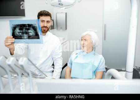 Felice elder donna durante la consultazione con bel dentista che mostra vedute x-ray nello studio dentistico Foto Stock