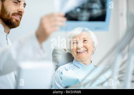 Felice elder donna durante la consultazione con bel dentista che mostra vedute x-ray nello studio dentistico Foto Stock