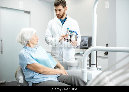 Dentista che mostra la ganascia artificiale durante la consultazione con il sambuco donna nello studio dentistico Foto Stock