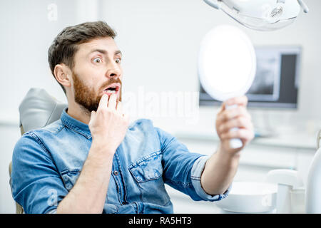 Ritratto di un uomo preoccupato con i suoi denti guardando sullo specchio nello studio dentistico Foto Stock
