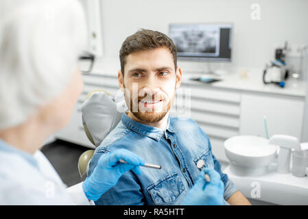 Uomo bello durante la consultazione dentale con donna anziana dentista in studio dentistico Foto Stock