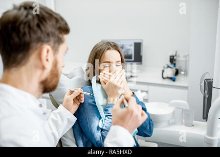 Donna con un spaventati espressione facciale durante una procedura stomatologiche con connettore maschio di tipo medico in studio dentistico Foto Stock