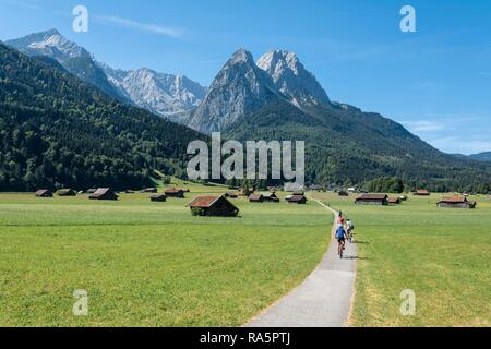 I ciclisti in tour in bici, pista ciclabile con mountain bike, dietro il massiccio dello Zugspitze, Tegernauweg, vicino a Grainau, attraversamento delle Alpi Foto Stock