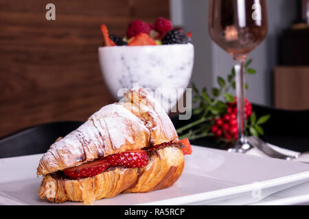 Stile Francese romantico picnic estivo impostazione. Flat-lay di bicchieri di vino rosato, fragole fresche, croissant, formaggio brie, cappello, occhiali da sole, peonia flo Foto Stock
