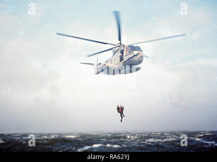 1977 - Un mare-vista aerea di un HH-3 Jolly gigante verde elicottero utilizzando un paranco di recupero per sollevare due pararescuemen dall'acqua al largo della costa della California. Gli uomini, dal 129Aerospace Rescue and Recovery Group della Air National Guard, partecipano in pratica una missione di salvataggio. Foto Stock