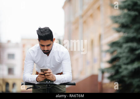 Uomo indiano utilizzando il telefono cellulare e il pignone fisso della bicicletta in strada. Foto Stock