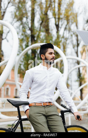 Felice l'uomo indiano vestito in camicia in piedi con una bicicletta su strada Foto Stock