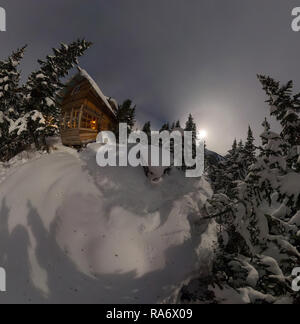 Vista aerea casa chalet durante una nevicata nel gli alberi della foresta di inverno di notte al chiaro di luna Foto Stock