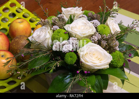 Bouquet di fiori con bianco ranuncolo ranunculus, Green Carnation e piccole viola e fiori bianchi su un tavolo di legno. La luce verde del foro della piastra punteggiata con frutta mela e pera Foto Stock