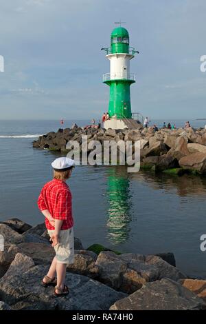 Ragazzo con un capitano del cappello, in piedi nella parte anteriore del Faro di Warnemunde, Rostock, Meclemburgo-Pomerania Occidentale, Germania Foto Stock