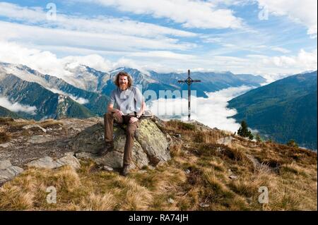 Escursionista, escursionista si siede sulle rocce, Kleiner Nock (2227 m) con la croce, Speikboden, vista in Valle Aurina, a Sand in Taufers, Campo Tures Foto Stock