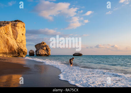 Paphos, Cipro - 24 Novembre 2018: un ragazzo scalzi suona presso la spiaggia di Petra tou Romiou rocce in Paphos, Cipro. La spiaggia è considerata a b Foto Stock