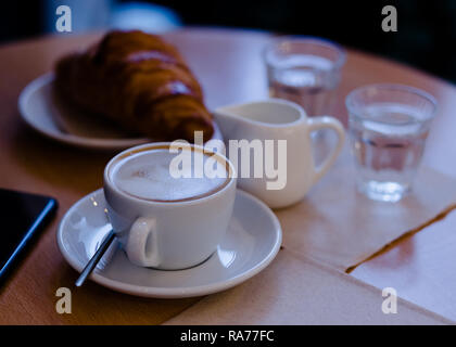 Croissant sulla piastra, caffè con latte, una pentola di latte e due bicchieri di acqua su un tavolo in un caffè di Parigi, Francia Foto Stock