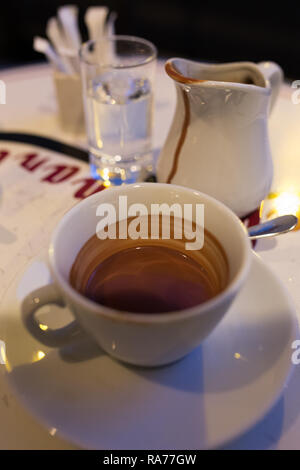 Una tazza di cioccolata calda e un bicchiere di acqua con una pentola di latte su un tavolo in un caffè di Parigi, Francia Foto Stock