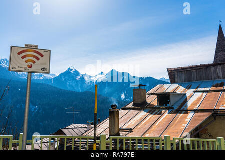 Zona di accesso Wifi, stagno, arrugginita tetto e montagne innevate sullo sfondo. Termenago, piccolo borgo nel comune di Pellizzano, Trento Italia Foto Stock