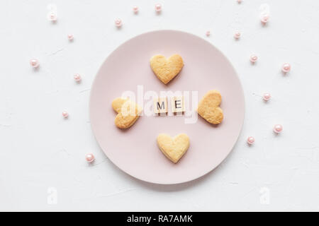 ME la parola e a forma di cuore biscotti al burro su una piastra di rosa e il giorno di San Valentino decorazione - pearles rosa su sfondo bianco Foto Stock