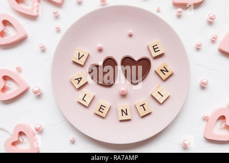 Parola di San Valentino e due Cuori di cioccolato su una piastra di rosa e il giorno di San Valentino - decorazione a forma di cuore ad luci su uno sfondo bianco Foto Stock