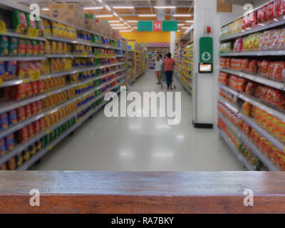 Svuotare tavolo in legno sulla parte superiore sfumata people shopping nella selezione di snack sul ripiano nel supermercato o department store, prodotti sugli scaffali Foto Stock