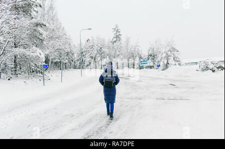 Lo stile di vita di viaggio. Giovane donna con zaino in inverno a piedi lungo la strada innevata in Svezia Foto Stock