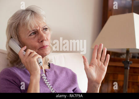 Senior donna indesiderate di ricezione chiamata telefonica a casa Foto Stock