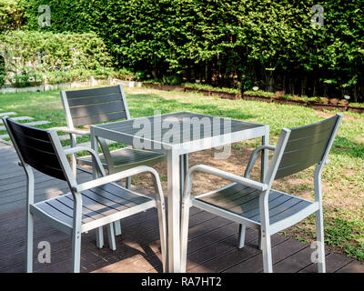 Moderno e di colore bianco e grigio tavolo da pranzo in legno set, tavolino quadrato e tre poltrone sulla terrazza in legno nel giardino verde. Foto Stock