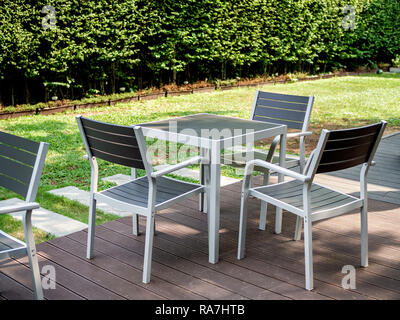 Moderno e di colore bianco e grigio tavolo da pranzo in legno set, tavolino quadrato e tre poltrone sulla terrazza in legno nel giardino verde. Foto Stock