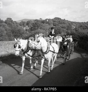 1967, mosso da un cavallo open-top nozze carrello tenendo la sposa e lo sposo e gli ospiti al ricevimento essendo riden lungo una strada di campagna, England, Regno Unito Foto Stock