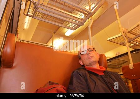 Un uomo anziano con gli occhiali il pendolarismo a lavoro. La mezza età uomo guardando fuori della finestra del treno. Passeggero durante il viaggio in alta velocità treno express in Foto Stock