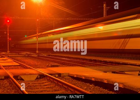 Bianco e blu treno passa una piccola scoperchiata stazione ferroviaria di notte nella Repubblica Ceca. Sfocata treno di movimento Foto Stock