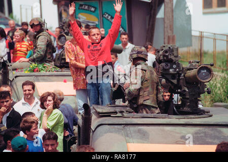 1999 - Ethenic albanesi si riuniscono in piazza per una parata tenutasi in onore delle forze americane in Kosovo villaggio di Koretin. I bambini salire sulla cima di un M998 High-Mobility multiuso di veicolo su ruote (HMMWV) con missili TOW. Foto Stock