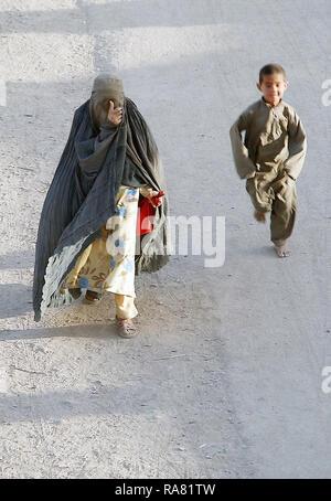 Un locale donna afghana, in un burqa, passeggiate lungo la strada mentre un ragazzo afgano corre dietro di lei nella città di Kandahar, Afghanistan. Questo è al di fuori del perimetro di Kandahar Air Base durante l'Operazione Enduring Freedom. Foto Stock