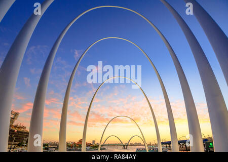 Perth, Western Australia - Jan 6, 2018: Elizabeth Quay Bridge al tramonto visto attraverso gli archi di Spanda scultura in Elizabeth Quay Marina. Spanda è stato progettato dal famoso artista Christian de Vietri. Foto Stock