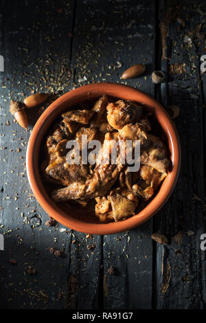 Angolo di alta vista di una casseruola di terracotta con alcuni pezzi di coniglio, di prugne e di funghi, tipicamente consumato in Spagna, il grigio di una tavola in legno rustico Foto Stock