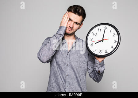 Ritratto di un uomo sorridente triste perchè tardi holding orologio da parete su sfondo grigio Foto Stock