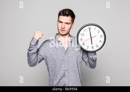 Ritratto di un sorridente uomo informale con la vittoria del gesto sul muro orologio su sfondo grigio Foto Stock