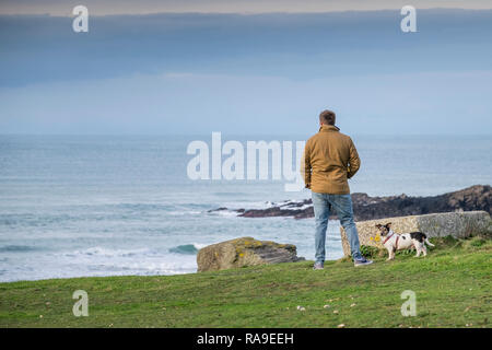 Un uomo in piedi con il suo Jack Russell Terrier sulla costa che guarda al mare. Foto Stock