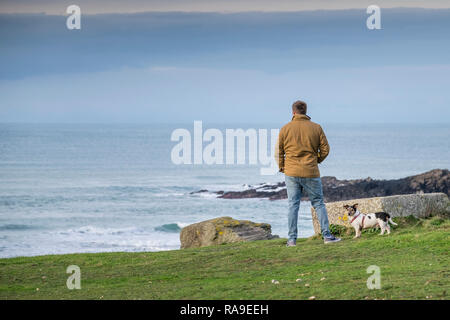 Un uomo in piedi con il suo Jack Russell Terrier sulla costa che guarda al mare. Foto Stock