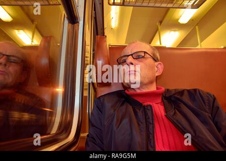 La mezza età uomo guardando fuori della finestra del treno. Passeggero durante il viaggio in alta velocità treno express in europa. Uomo anziano che viaggiano in treno di sera Foto Stock