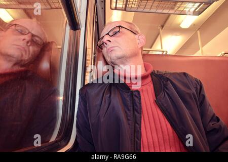 La mezza età uomo guardando fuori della finestra del treno. Passeggero durante il viaggio in alta velocità treno express in europa. Uomo anziano che viaggiano in treno di sera Foto Stock